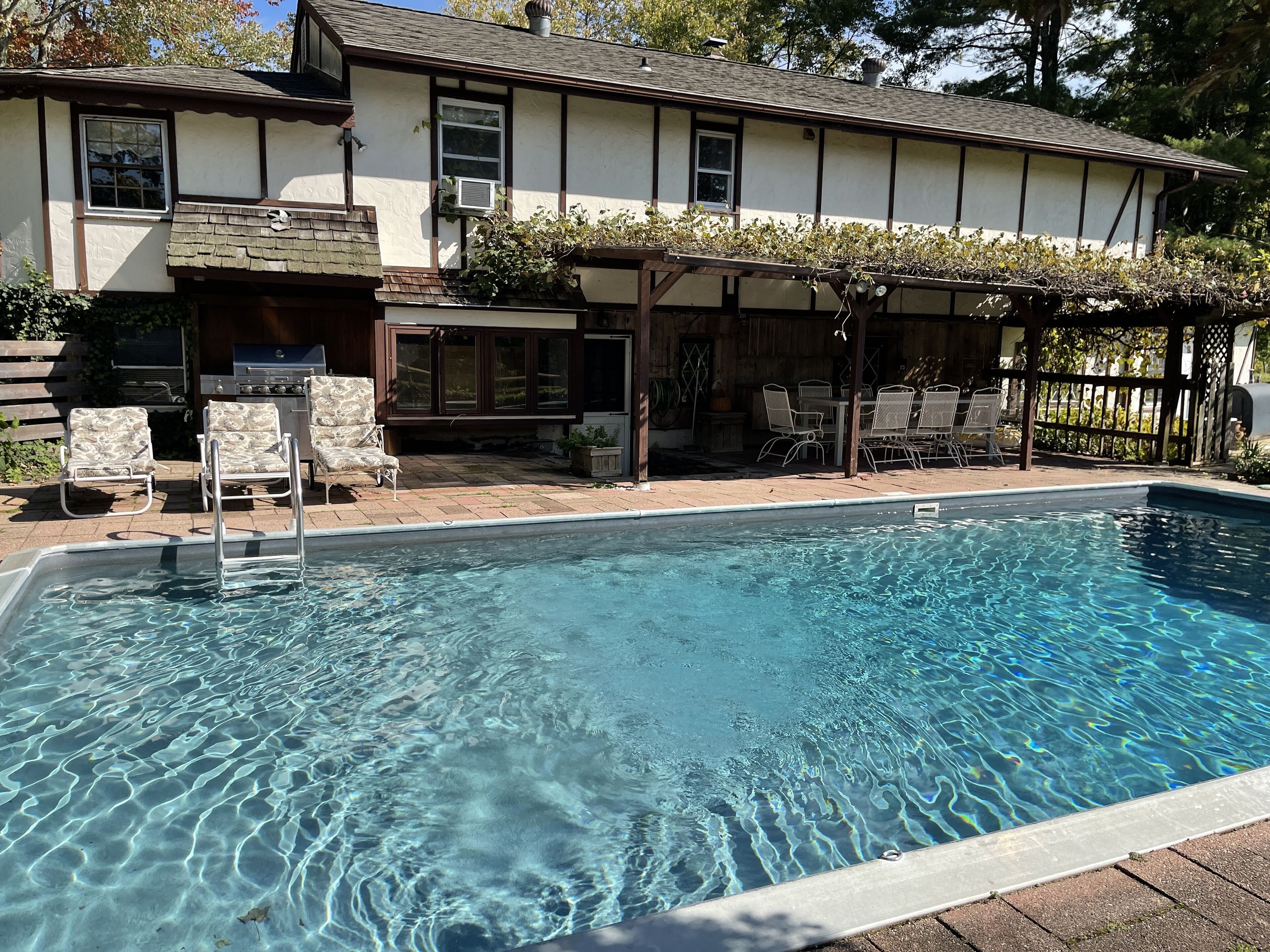 Une piscine à l’eau claire, entourée d’une terrasse en bois et de mobilier d’extérieur.