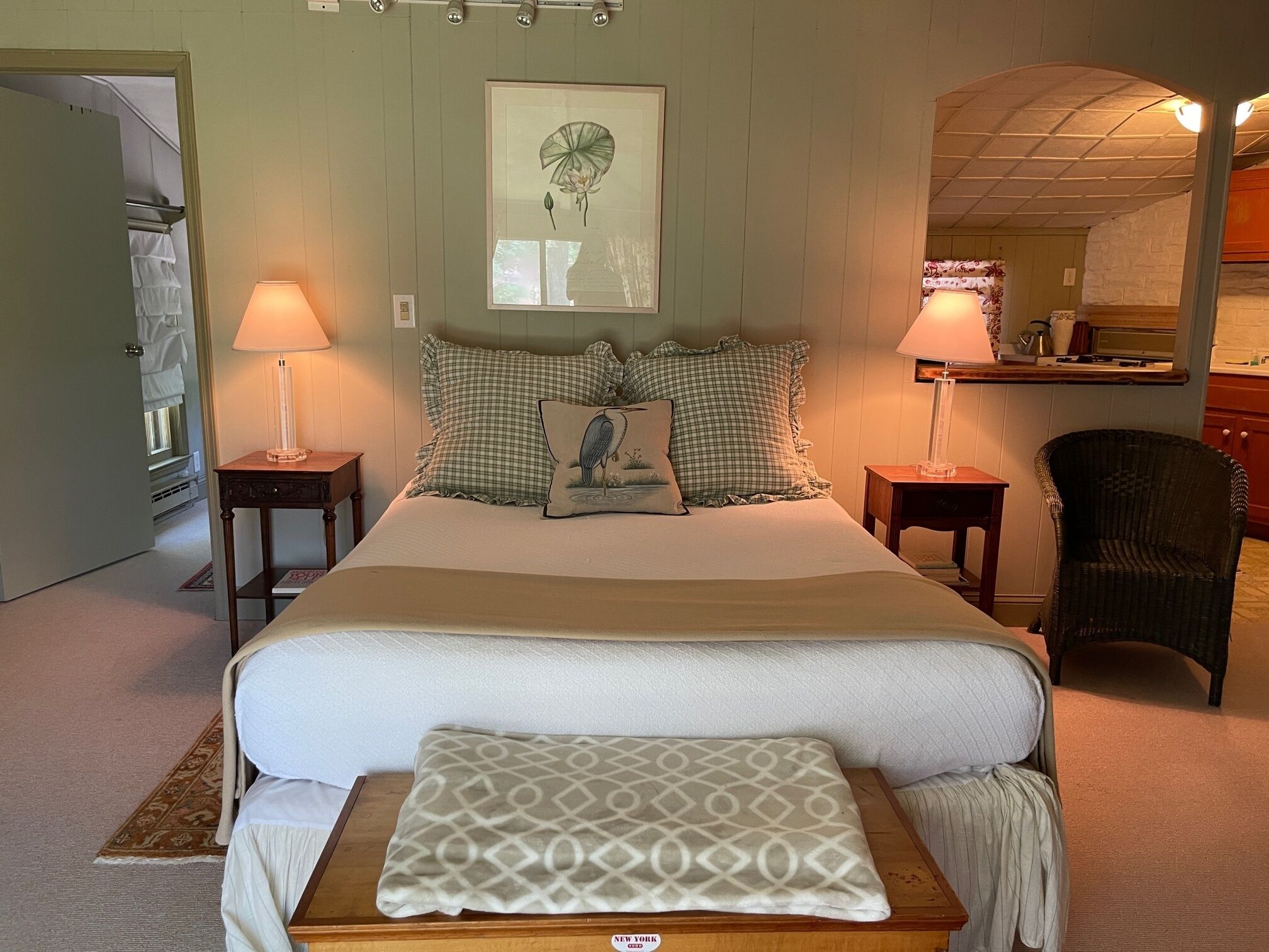 A bedroom with a bed, two bedside tables, a chair, a mirror, and a framed picture on the wall.