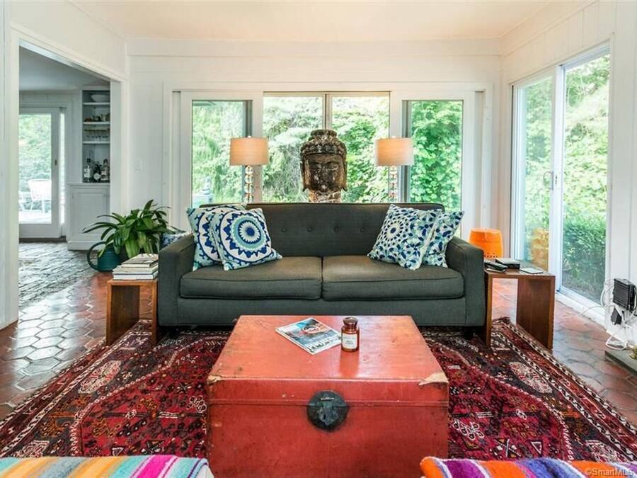 A living room with a grey sofa, patterned cushions, a red trunk, and a Buddha statue.