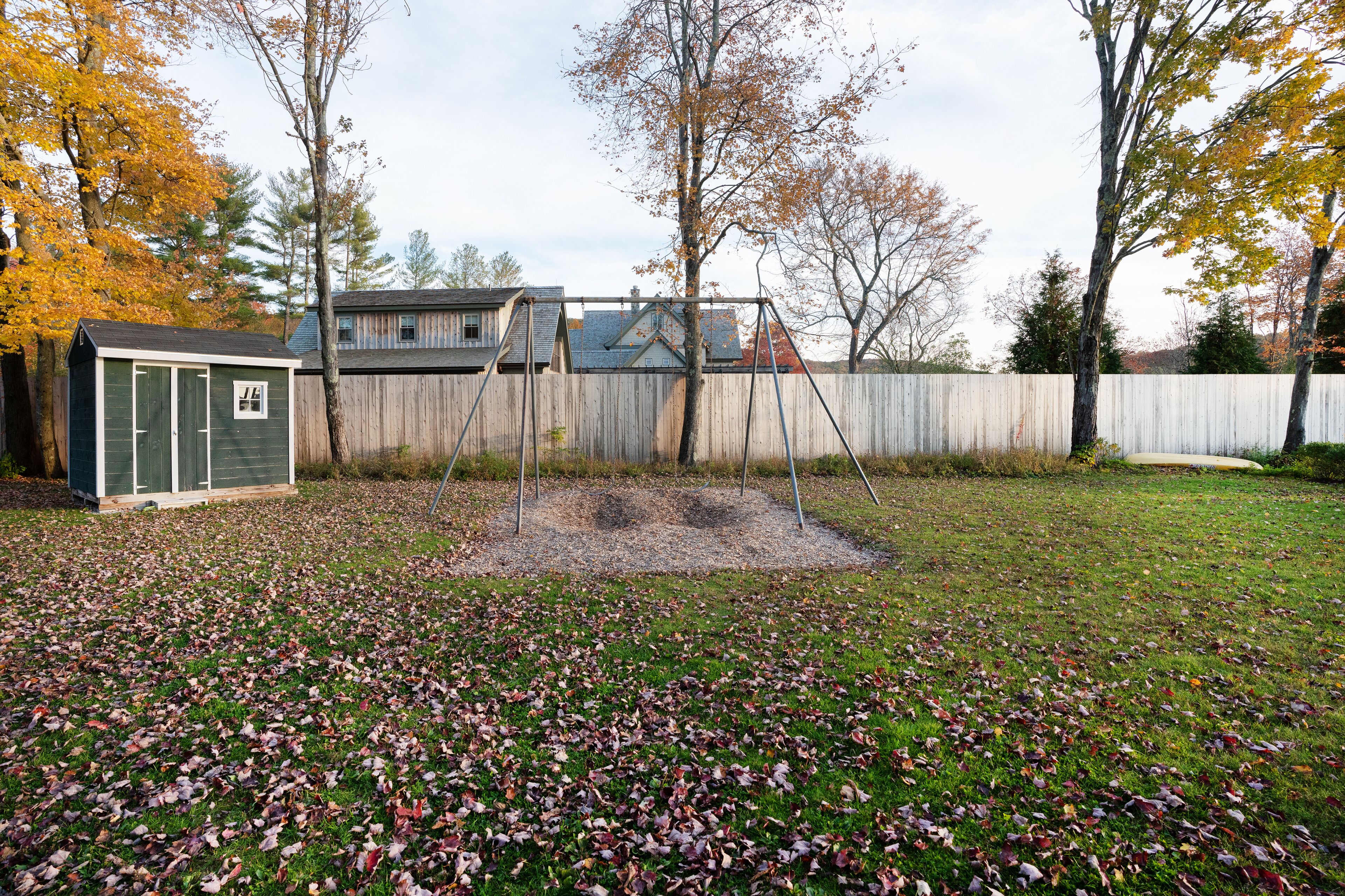 A backyard with a swing set, a shed, and a wooden fence.