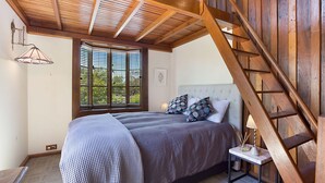 A bedroom with a bed, a window with blinds, a bedside table with a lamp, and a wooden staircase. - 10 Harper Crescent Narooma (Narooma)
