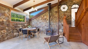 A stone-walled room with a wooden staircase, a table with chairs, and a wood-burning stove. - 10 Harper Crescent Narooma (Narooma)