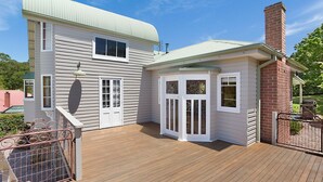 A two-story house with a wooden deck and a brick chimney. - 10 Harper Crescent Narooma (Narooma)