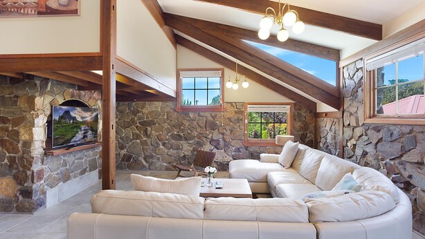 A spacious living area with a stone fireplace, a large sectional sofa, and a view of the outdoors through a skylight. - 10 Harper Crescent Narooma (Narooma)