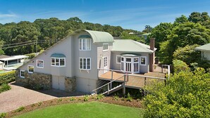 A two-story house with a green roof, a stone foundation, and a wooden deck. - 10 Harper Crescent Narooma (Narooma)