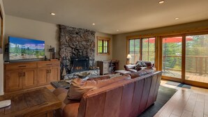 Una sala de estar amplia con chimenea de piedra, sofá de cuero y televisor sobre un mueble de madera.