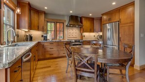 Una cocina moderna con armarios de madera, un refrigerador de acero inoxidable, horno empotrado y un comedor con mesa y sillas de madera.