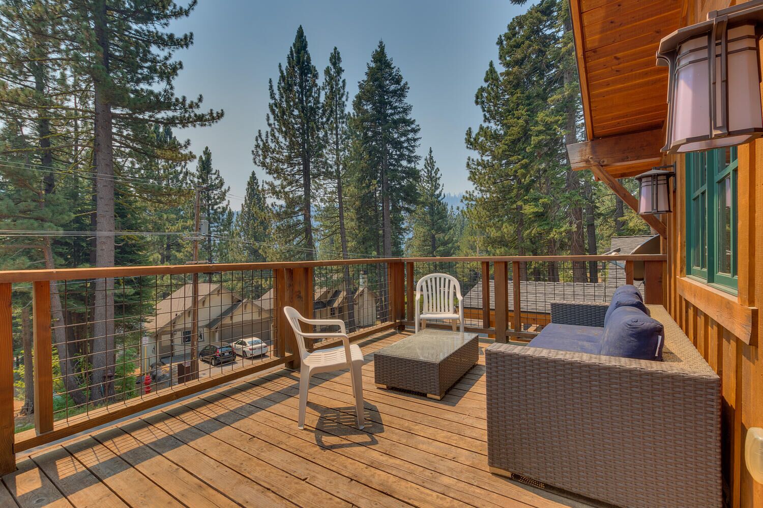 A wooden deck with wicker furniture, a white chair, and a view of a forested area.