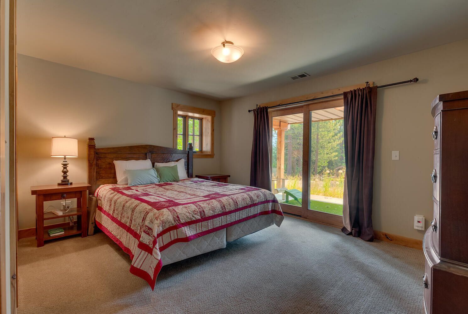 Un dormitorio con una cama grande, una mesita de noche, una lámpara, una ventana con cortinas y vistas al exterior.