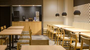Un restaurante con mesas y sillas de madera, una barra con máquinas de café e iluminación colgante.