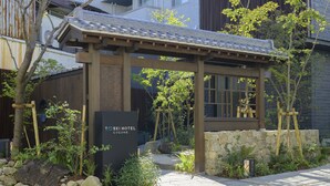 Una entrada tradicional al estilo japonés con una pérgola de madera, un camino de piedra y un letrero que indica el Hotel Tosei Cocoon.