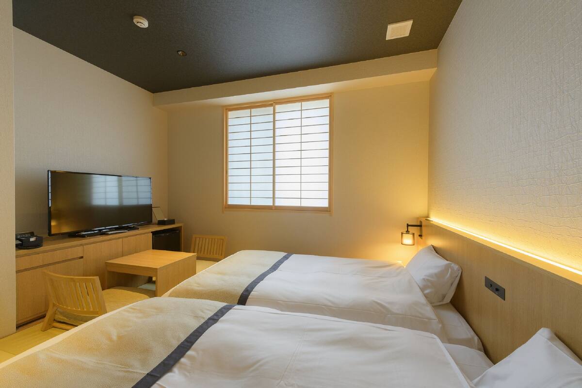 Une chambre d’hôtel avec deux lits, une télévision, un bureau et une fenêtre avec des stores.