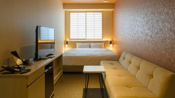 Habitación de hotel compacta con cama, sofá, escritorio con televisor y ventana que proporciona luz natural.