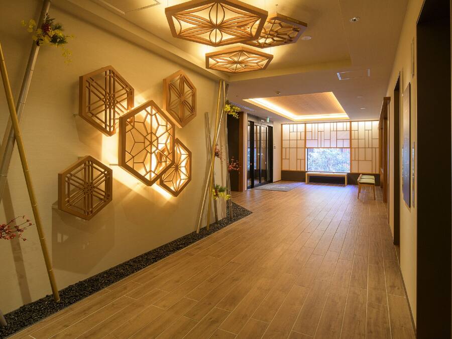 A hallway with wooden flooring, decorative wall sconces, and a bench.