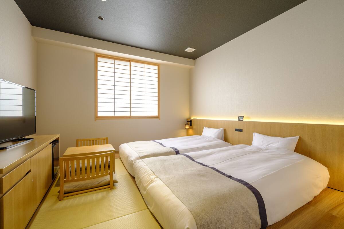 Une chambre d’hôtel avec deux lits, une télévision, une petite table et une fenêtre.