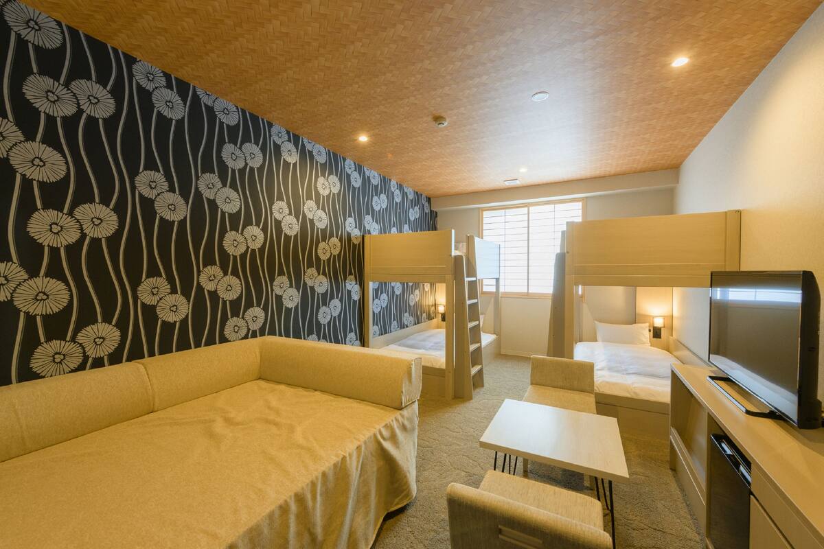 Une chambre d’hôtel avec un lit superposé, un canapé, une télévision et un bureau.