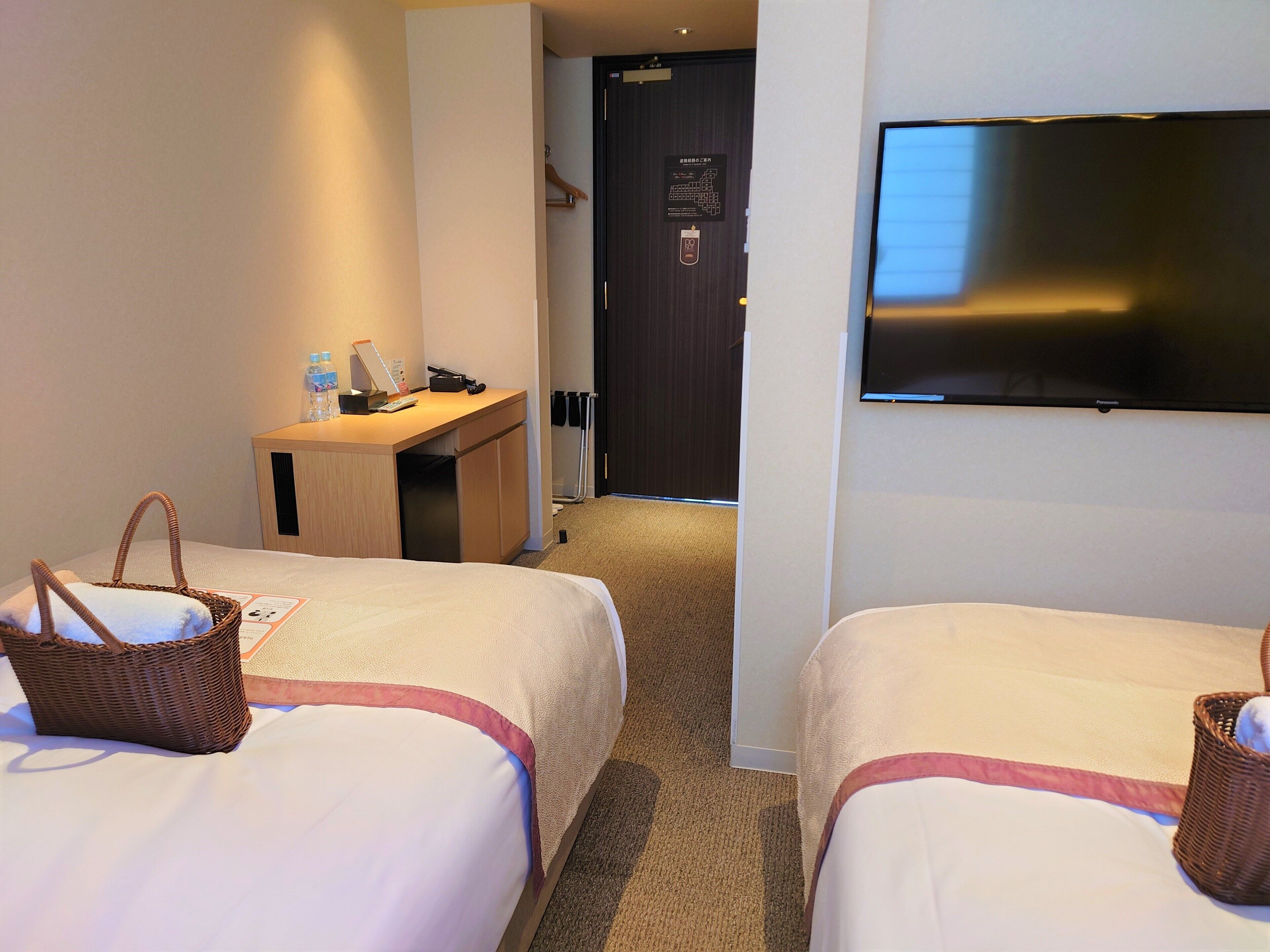 Habitación de hotel con dos camas, un escritorio, un televisor y una puerta.