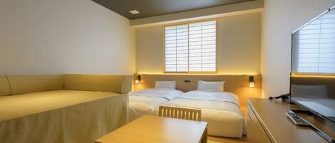 A compact hotel room with a sofa, two single beds, a small table, and a TV.