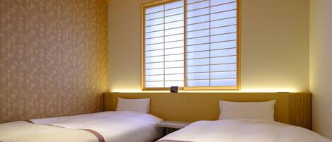 Ein Hotelzimmer mit zwei Betten, einem großen Fenster mit Jalousien und einem Wandteppich an einer Wand.