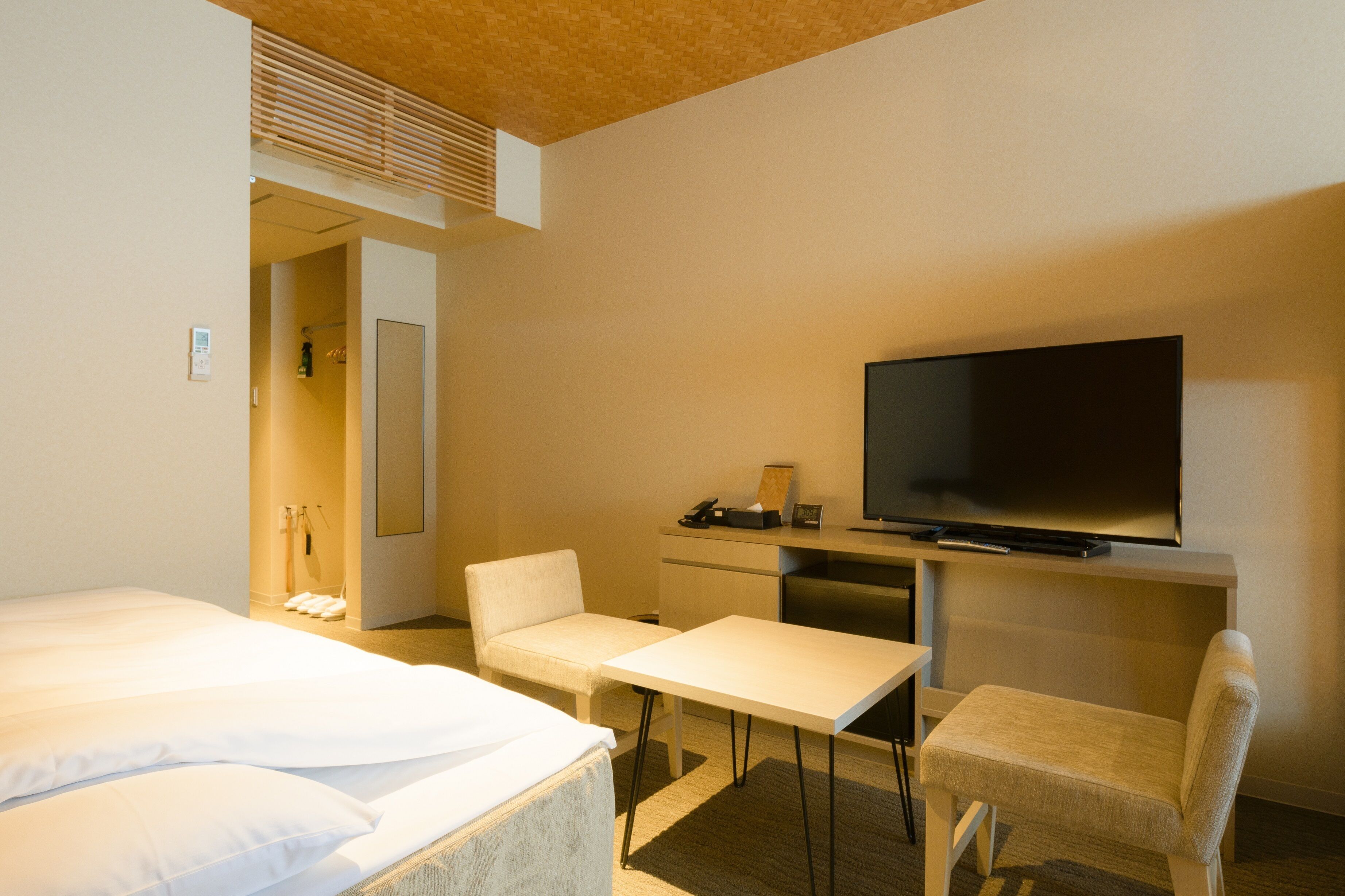 A hotel room with a bed, a desk, a chair, a television, and a shower area.