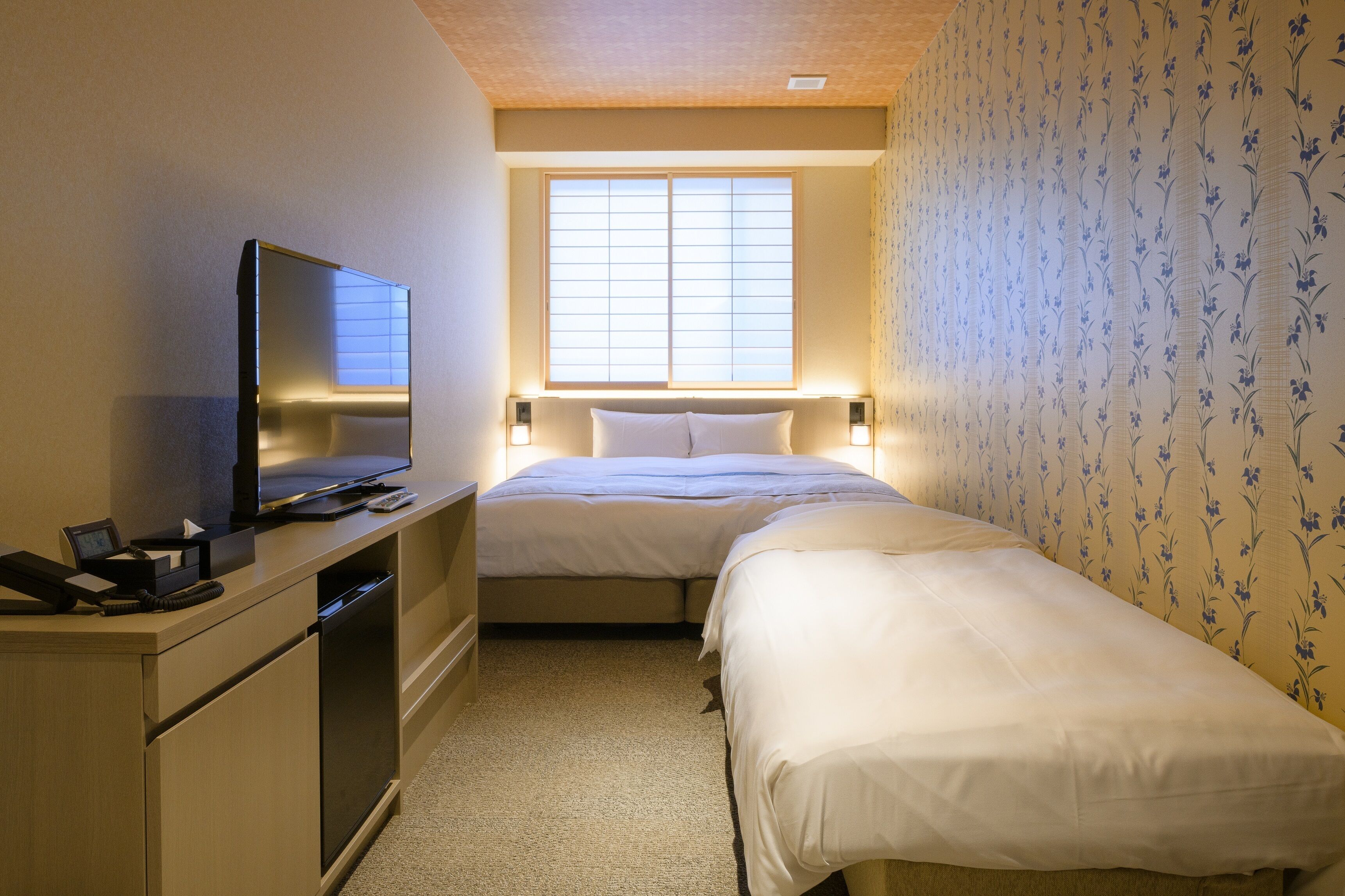 A hotel room with a bed, a desk with a television, and a window with blinds.