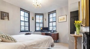 Cozy retreat with a large bed, desk, and fireplace, featuring large windows and a chandelier.