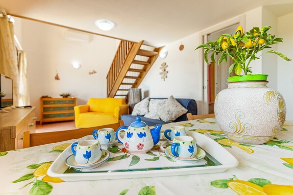 A dining area with a table set for tea, a vase with yellow flowers, and a staircase in the background. - Gli Ulivi Palau - Lu Maccioni Holiday Home with Wi-Fi, A/C, Terraces & Garden (Palau)