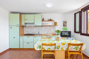 A kitchen with light green cabinets, a tiled backsplash, a table with a lemon tablecloth, and a microwave. - Gli Ulivi Palau - Lu Maccioni Holiday Home with Wi-Fi, A/C, Terraces & Garden (Palau)