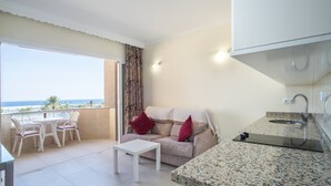 A balcony with a view of the sea, a sofa with red cushions, a small table, and a kitchen area with a granite countertop. - Marina View Modern Apartment with Sea View, Wi-Fi, A/C & Terrace (Fuengirola)