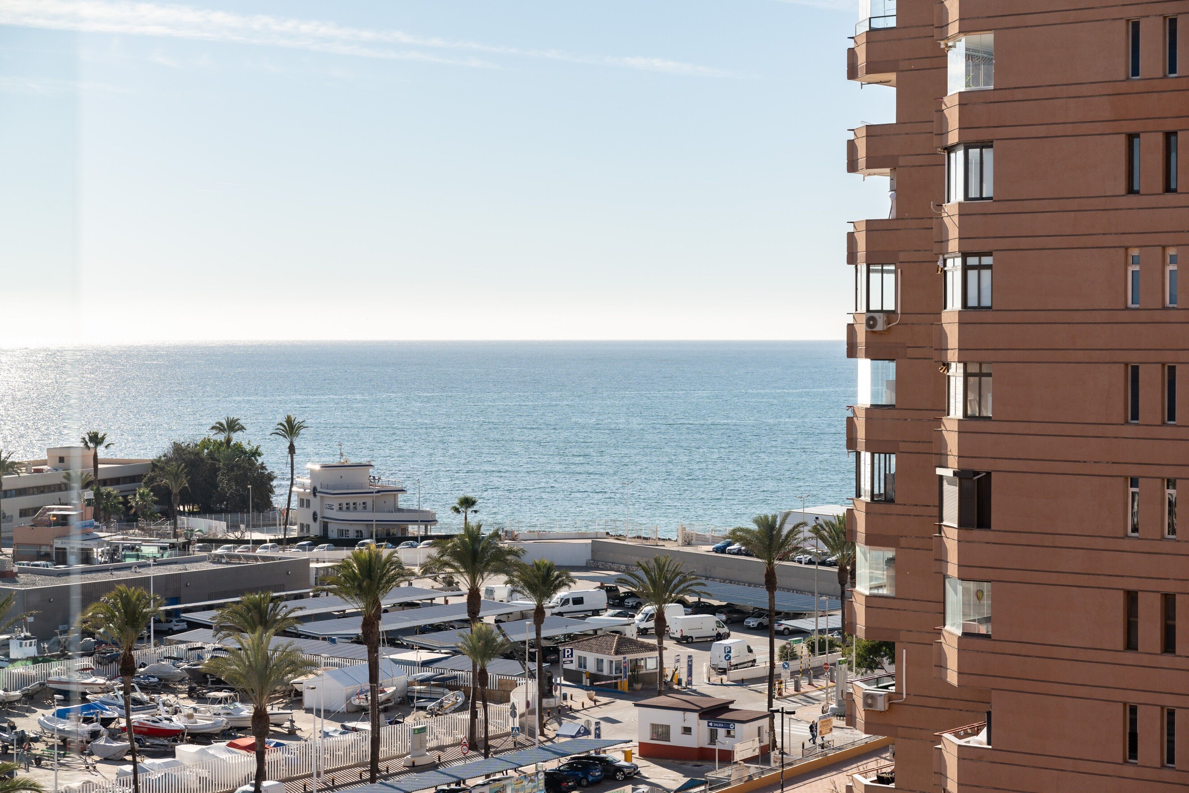 A coastal urban area with a view of the sea, buildings, and parked vehicles.