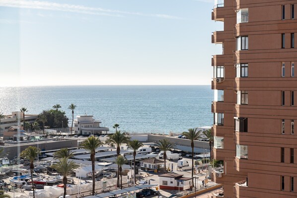A coastal urban area with a view of the sea, buildings, and parked vehicles.