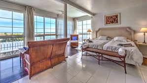 Habitación de hotel con una cama grande, un banco, una silla y vista a la playa.