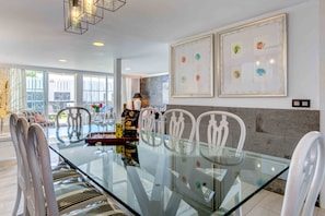 Uma sala de jantar moderna com mesa de vidro, cadeiras brancas e obras de arte emolduradas na parede.