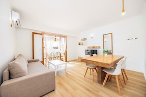 A modern living room with a sofa, dining table, chairs, and a kitchen area.