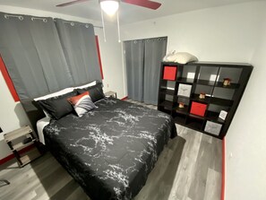 A bedroom with a bed, a nightstand, a ceiling fan, a wardrobe, and a shelf with decorative items.