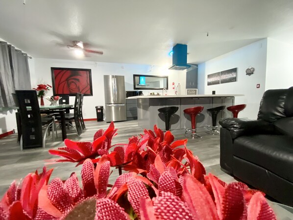 A modern kitchen with a stainless steel refrigerator, a dining area with a glass table, and a black leather sofa.