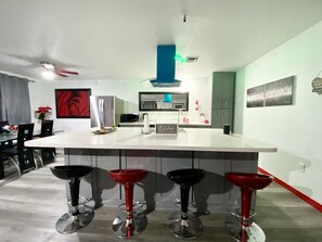 A modern kitchen with a central island, bar stools, and a dining area with a glass table and chairs.
