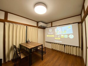 A conference room with a wooden table, chairs, a projector screen displaying a presentation, and a ceiling light.