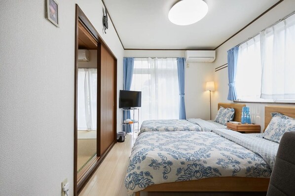 A hotel room with two beds, a TV, a bedside table, a lamp, and a window with curtains.