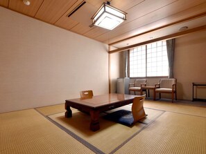 Ein traditioneller japanischer Raum mit Tatami-Bodenbelag, einem niedrigen Holztisch, zwei Stühlen und einem Fenster mit Vorhängen.