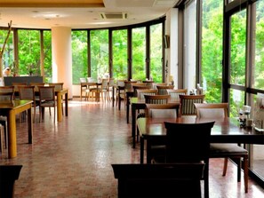 Enjoy meals in a spacious dining area with a high ceiling and large windows offering views of lush greenery.