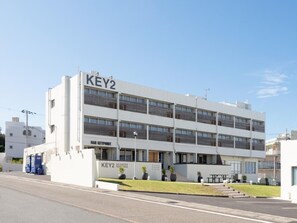 Un hotel KEY2 moderno con estructura de dos pisos, techo plano y entrada visible con un pequeño espacio de estar al aire libre.