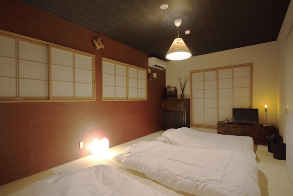 A traditional Japanese-style room with tatami flooring, a futon bed, sliding shoji doors, and a ceiling fan.