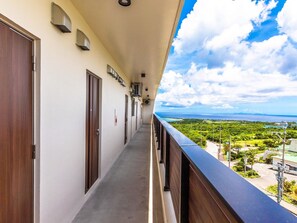 Ein Korridor mit Türen, ein Balkon und Blick auf eine Landschaft mit Grünflächen und einem Gewässer.