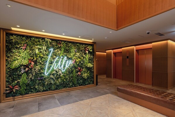 A lobby with a green wall featuring a neon sign, a bench, and a hallway with wooden doors.
