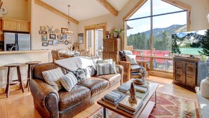 A spacious living room with a leather sofa, wooden coffee table, and a large window offering a mountain view.