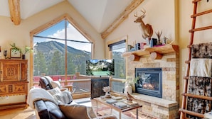 A cozy living room with a fireplace, leather sofa, and a large window overlooking a mountainous landscape.