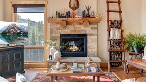 A cozy living room with a fireplace, books, a mounted deer head, and a ladder.
