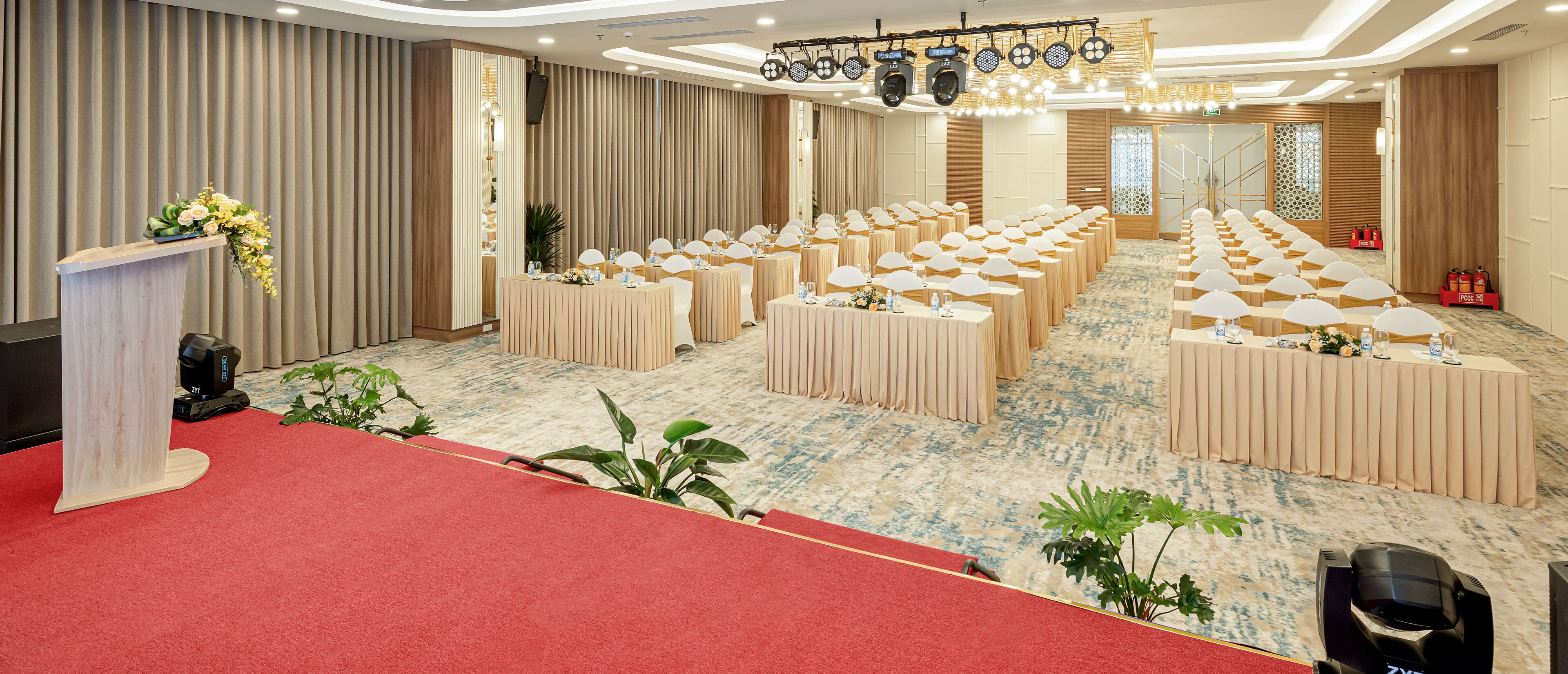 Un salón de conferencias con filas de mesas, un atril y una alfombra roja.