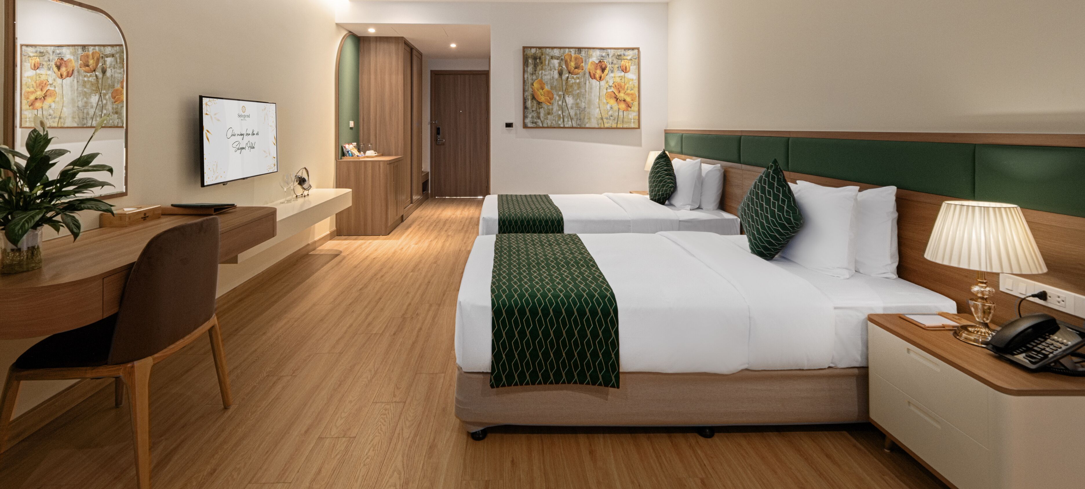 Habitación de hotel con dos camas, un escritorio, una silla, un televisor y obras de arte en las paredes.